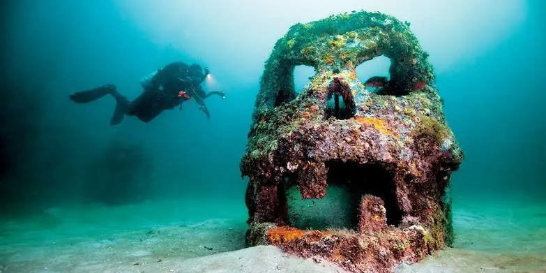 A scuba diver swims behind an artistic skull-shaped memorial reef sculpture colonized by marine life.
